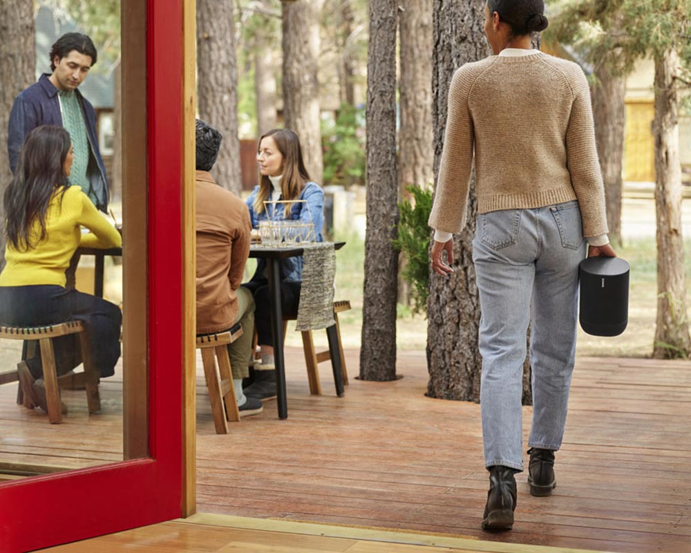 Group of people eating outside while a woman brings a portable sonos speaker